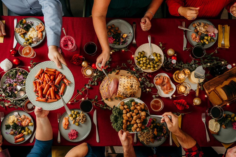 Bild direkt ovanför av flera som äter av ett traditionellt julbord med röd duk